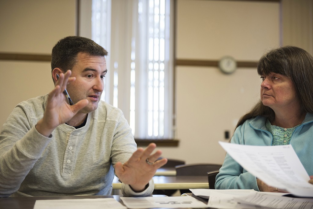 A photo of two colleagues at a table having a conversation, one with papers in hand.