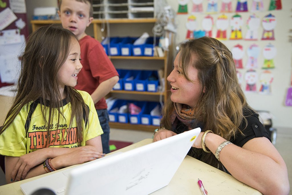 A college student interacting with a young student in a classroom setting.