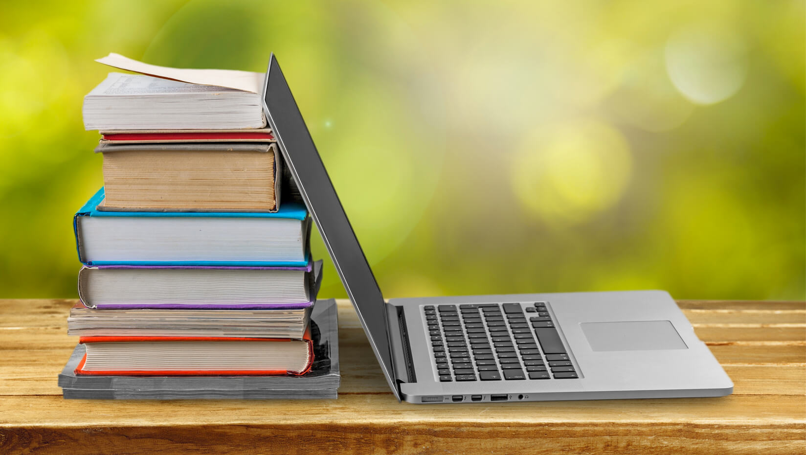 Stock photo of a laptop, its lid opened against a stack of books