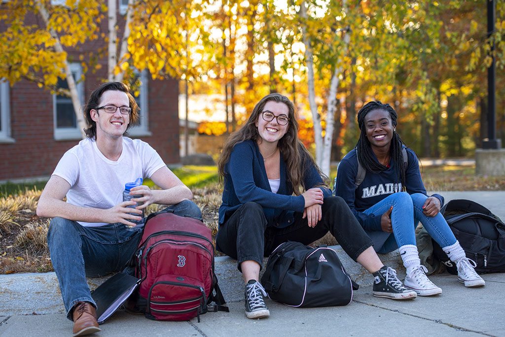 A photo of three students sitting outside with their book bags.