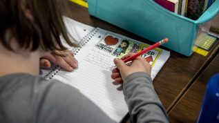 A photo looking over the shoulder of a student writing in a notebook