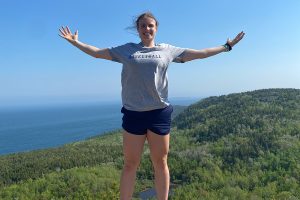 Ally Johnson poses with her arms outstretched in an outdoor setting.