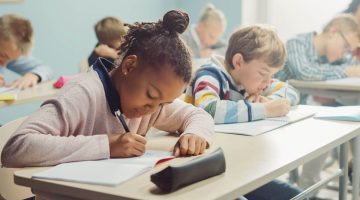 A photo of a classroom of diverse students practicing writing.