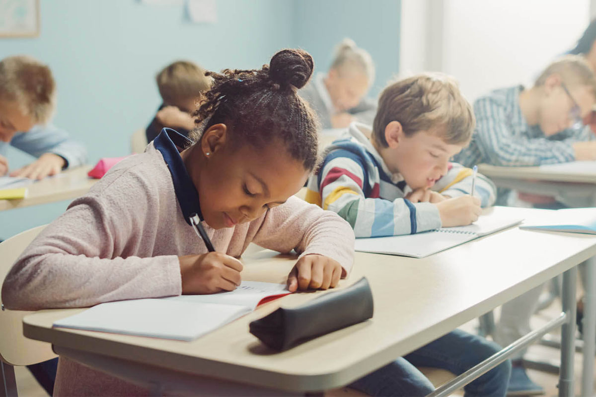 A photo of a classroom of diverse students practicing writing.