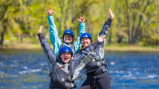 A group of UMaine students in a paddling safety course celebrate with their arms raise in the air.
