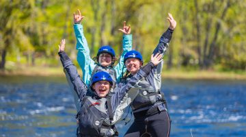 A group of UMaine students in a paddling safety course celebrate with their arms raise in the air.