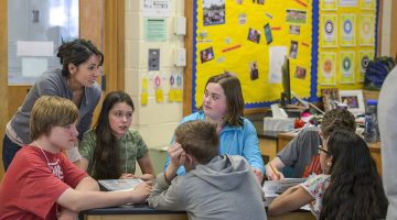 A teacher works with a group of middle school students on a tabletop activity.