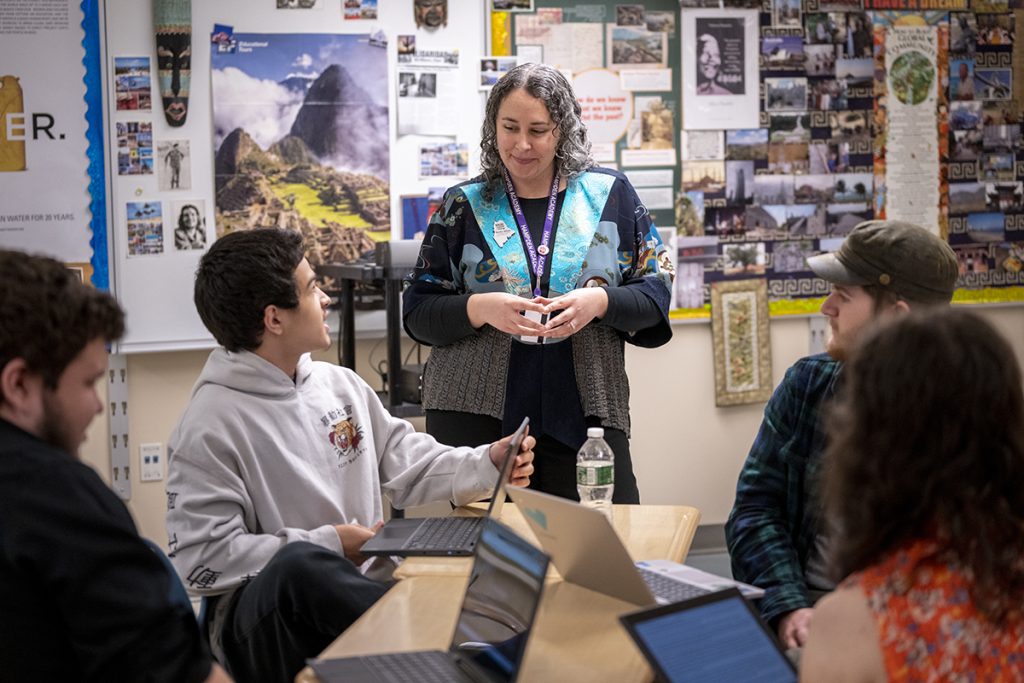 A photo of a teacher talking to a group of high school students.
