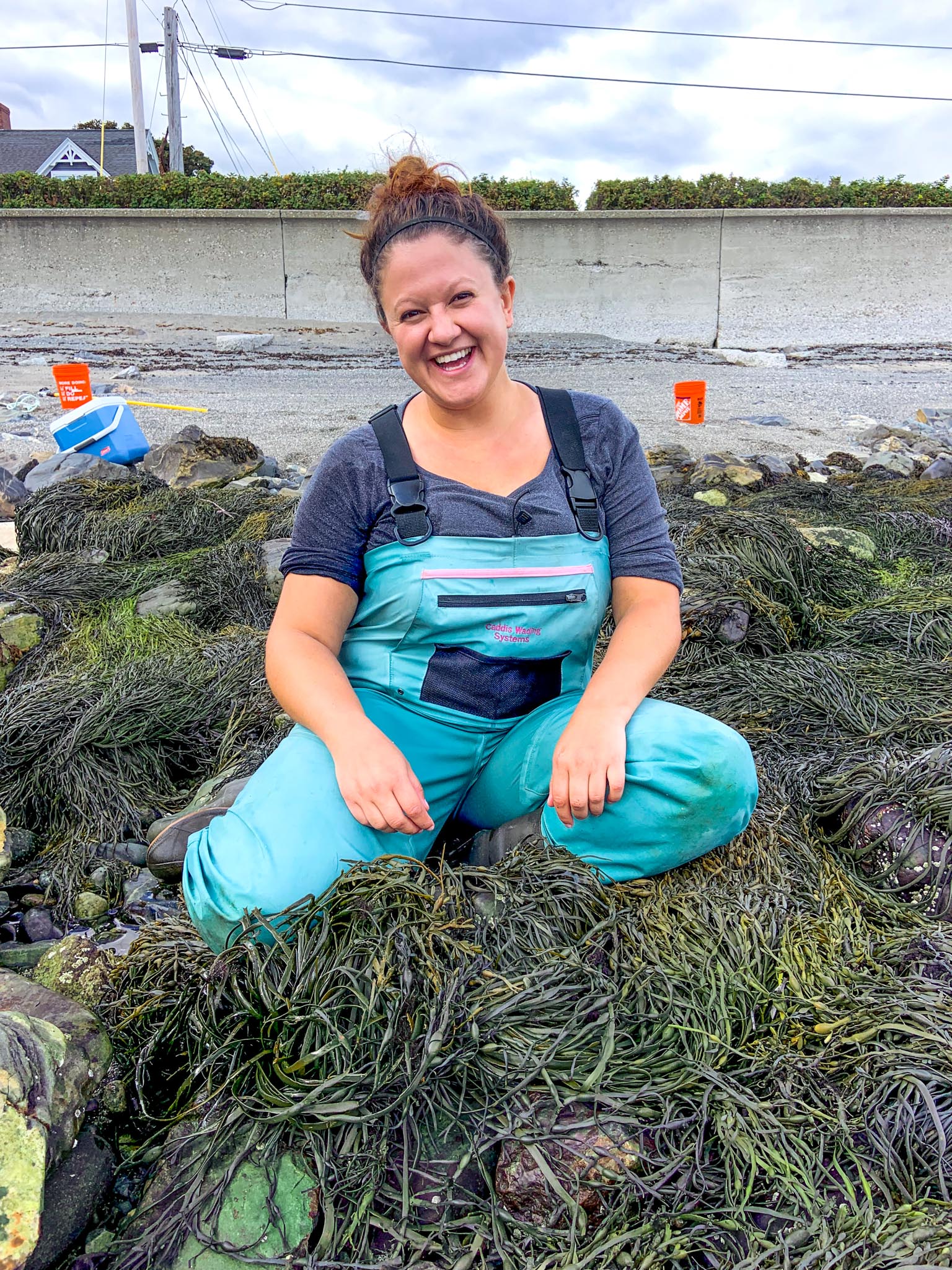 Emily Pierce sits in portrait on seaweed in front of a Jersey barrier