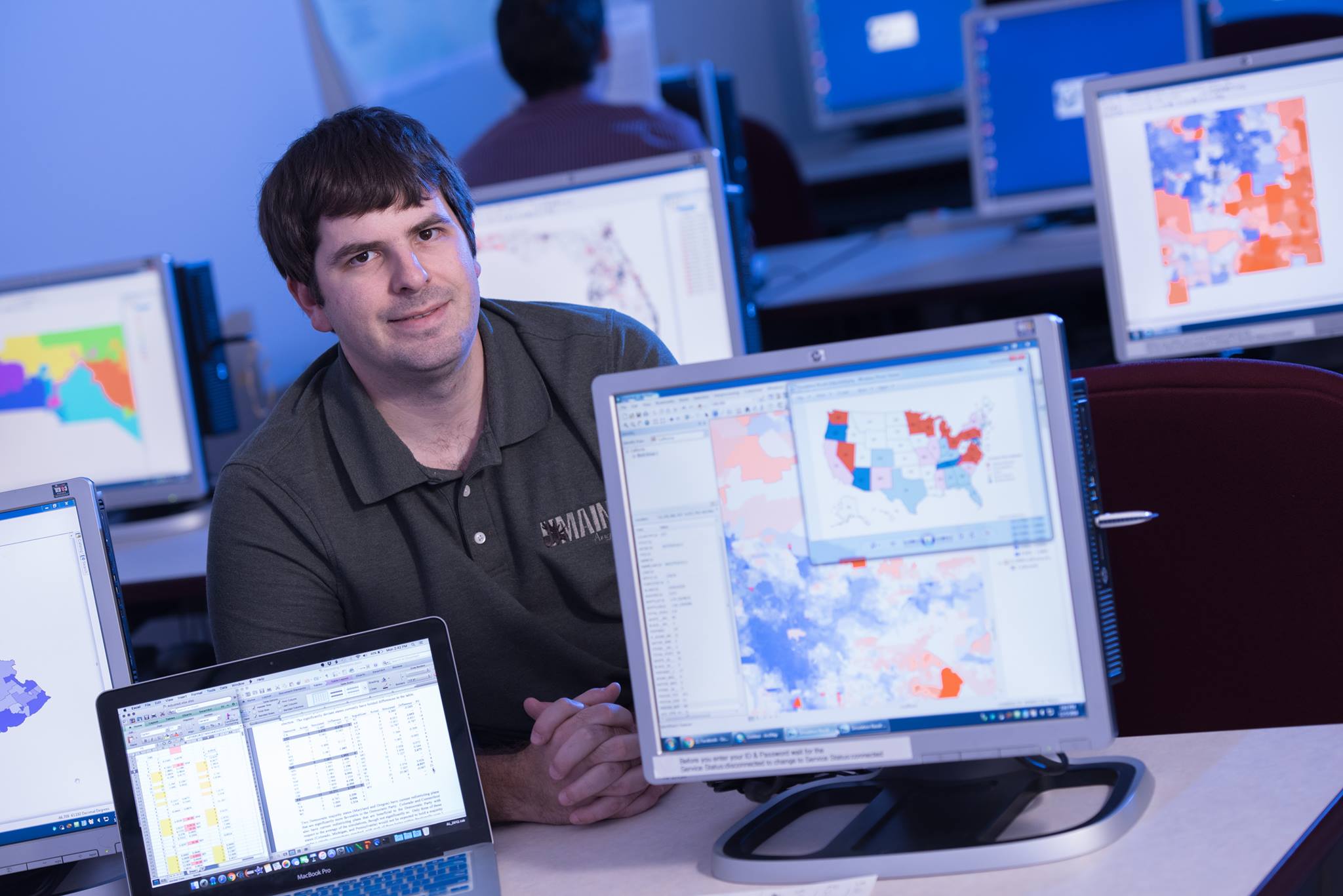 Matt Dube sits in computer lab with GIS maps on the screen.