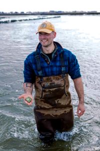 Adam Copeland stands knee-deep in water holding mussels