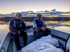 Two individuals sit in boat with seining nets.