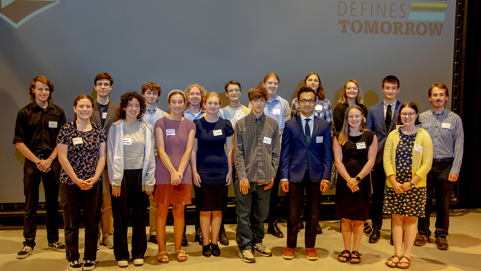 Group of students stand in two rows at front of presentation.