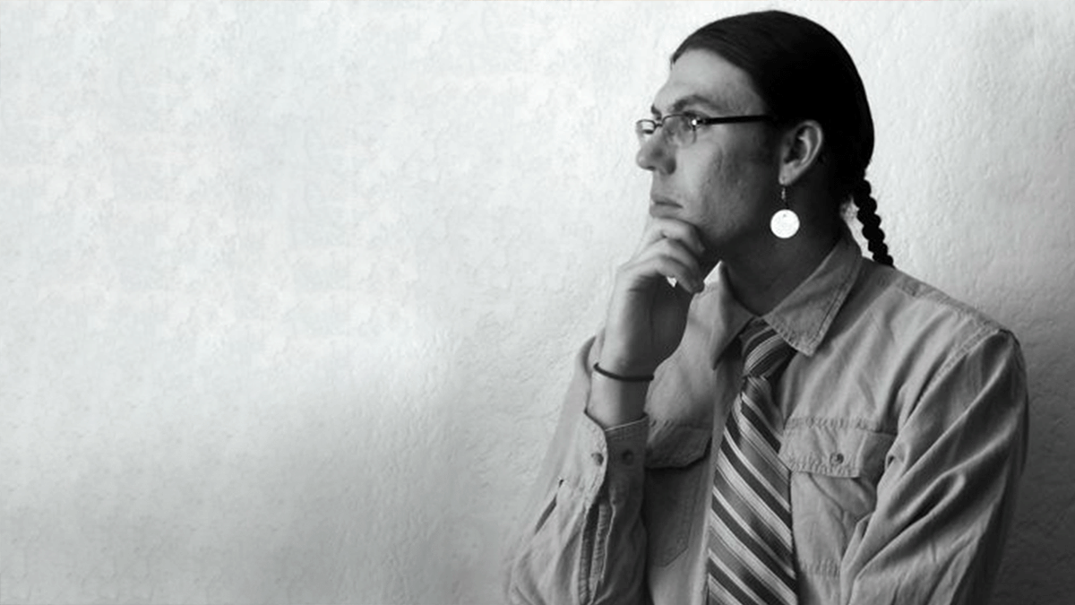 Man with braided hair stares off to the left.