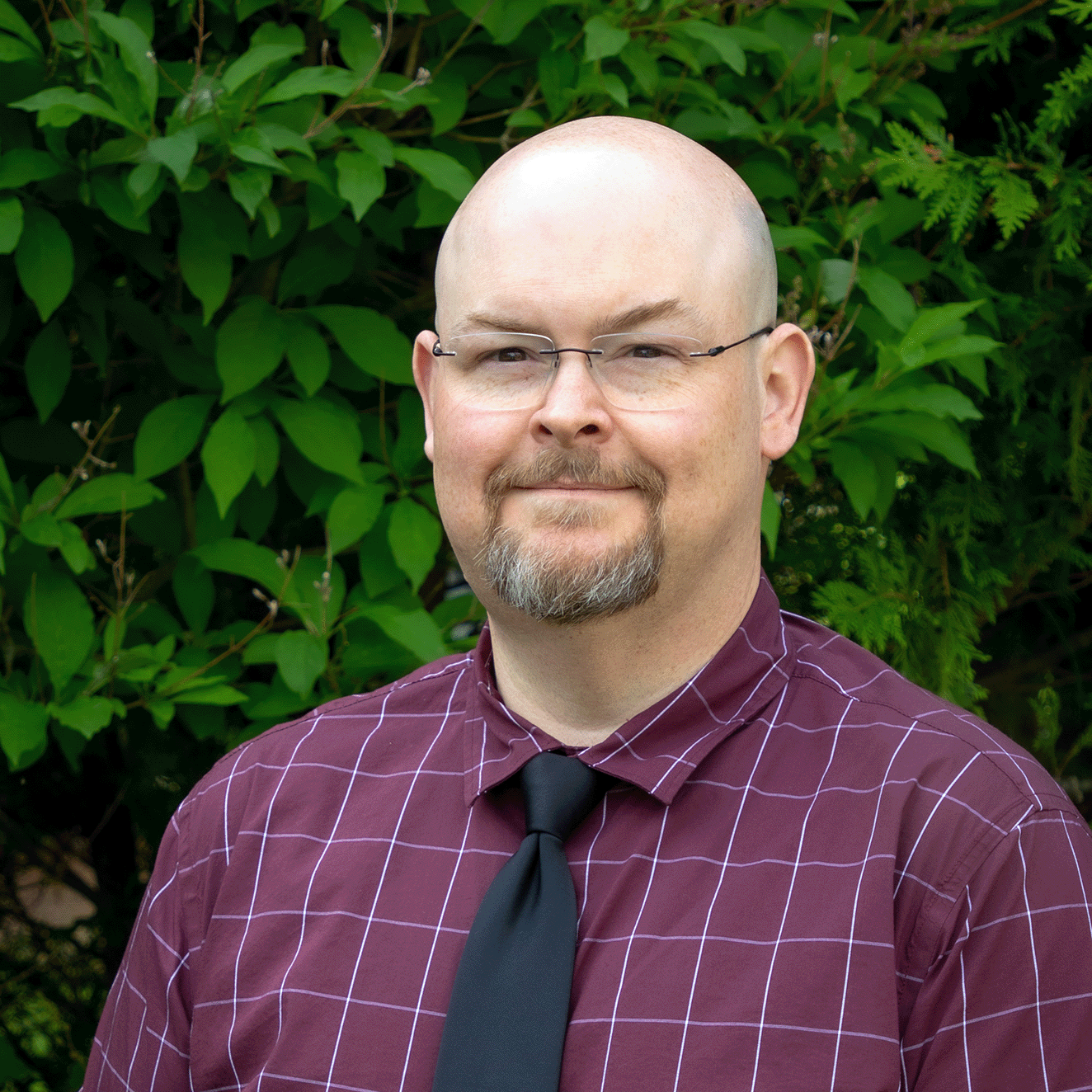 headshot of bald man with beard wearing a dark purple shirt and dark tie