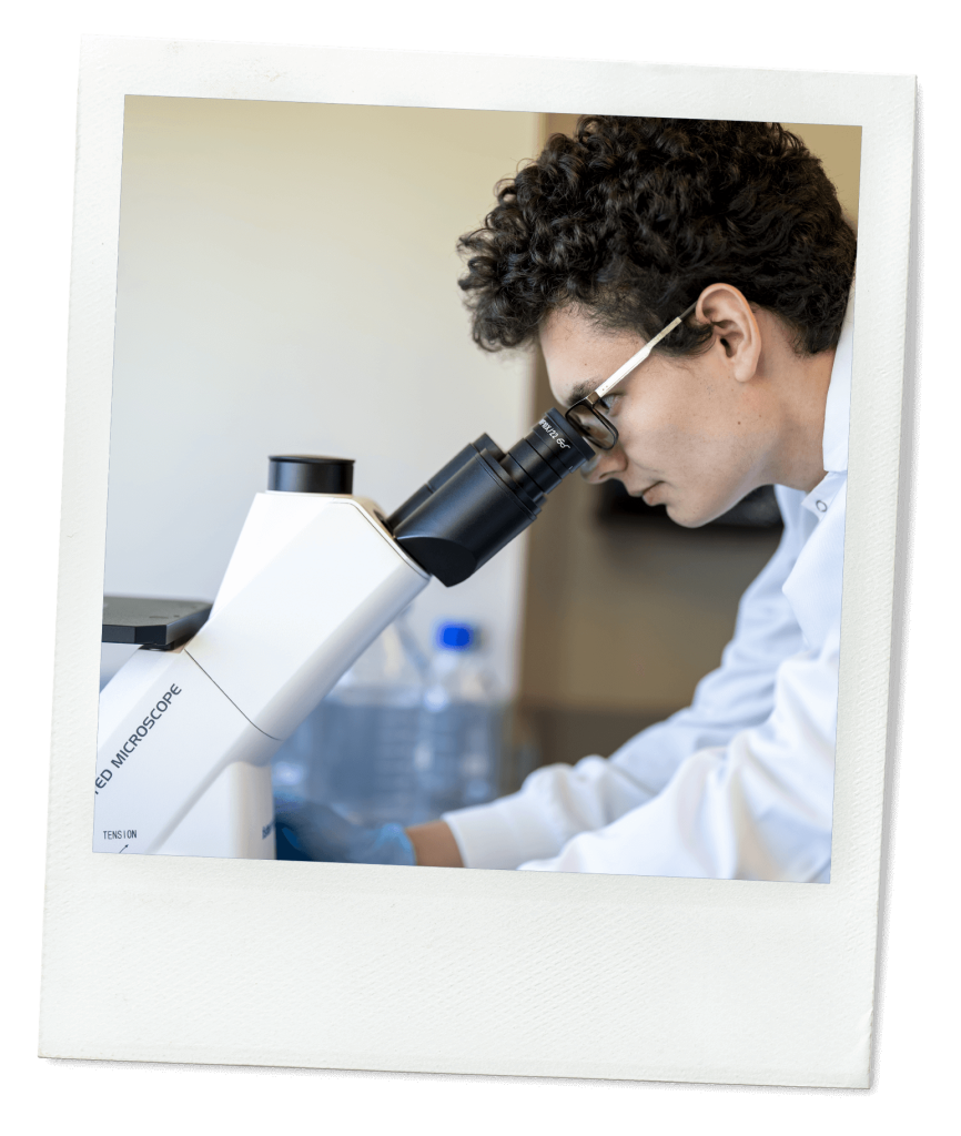 A photo of a student wearing a lab coat and looking into a microscope