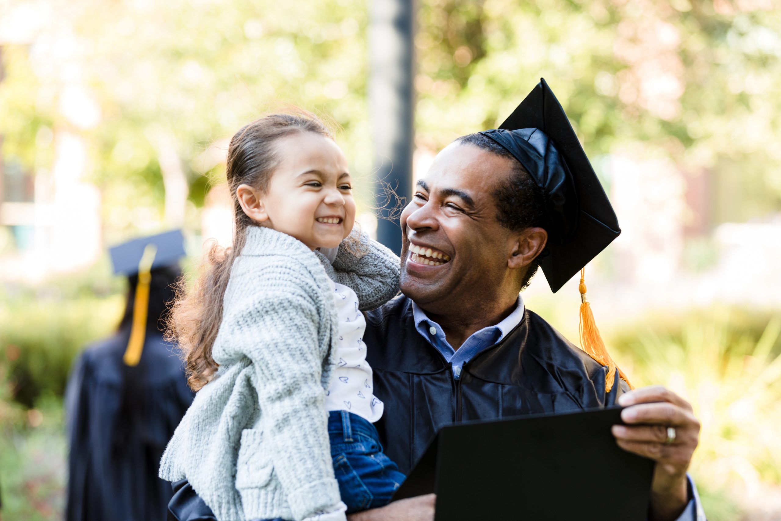 Adult in cap and gown holding a child and diploma