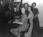 P08212: Group of women gathered around a telephone switchboard. Women telephone operators.
