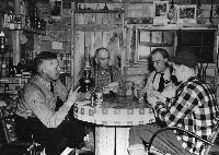 P00879: Four men playing cards around table in woods camp.
