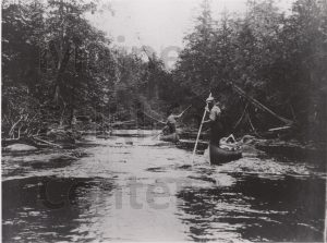P00293 Two men poling canoes up rips, c. 1914.