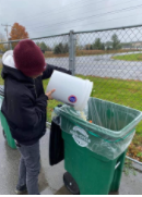 picture of a person pouring food waste from a 5 gallon bucket into a green transfer station food recycling bin