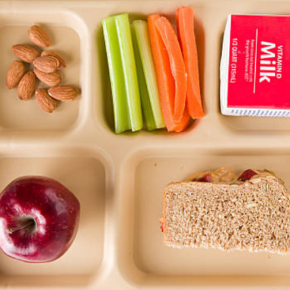 Photo of a cafeteria food tray with almonds, celery and carrots, milk, apples, and a sandwich.