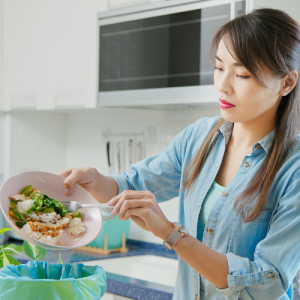 Image of a woman separating food waste off her plate into a container