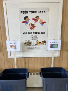 Poster designed by student intern, Eddie Nachamie, in Sebago Elementary School cafeteria near food waste sorting stations. Poster reads, "Feed your Body! Not the Trach"
