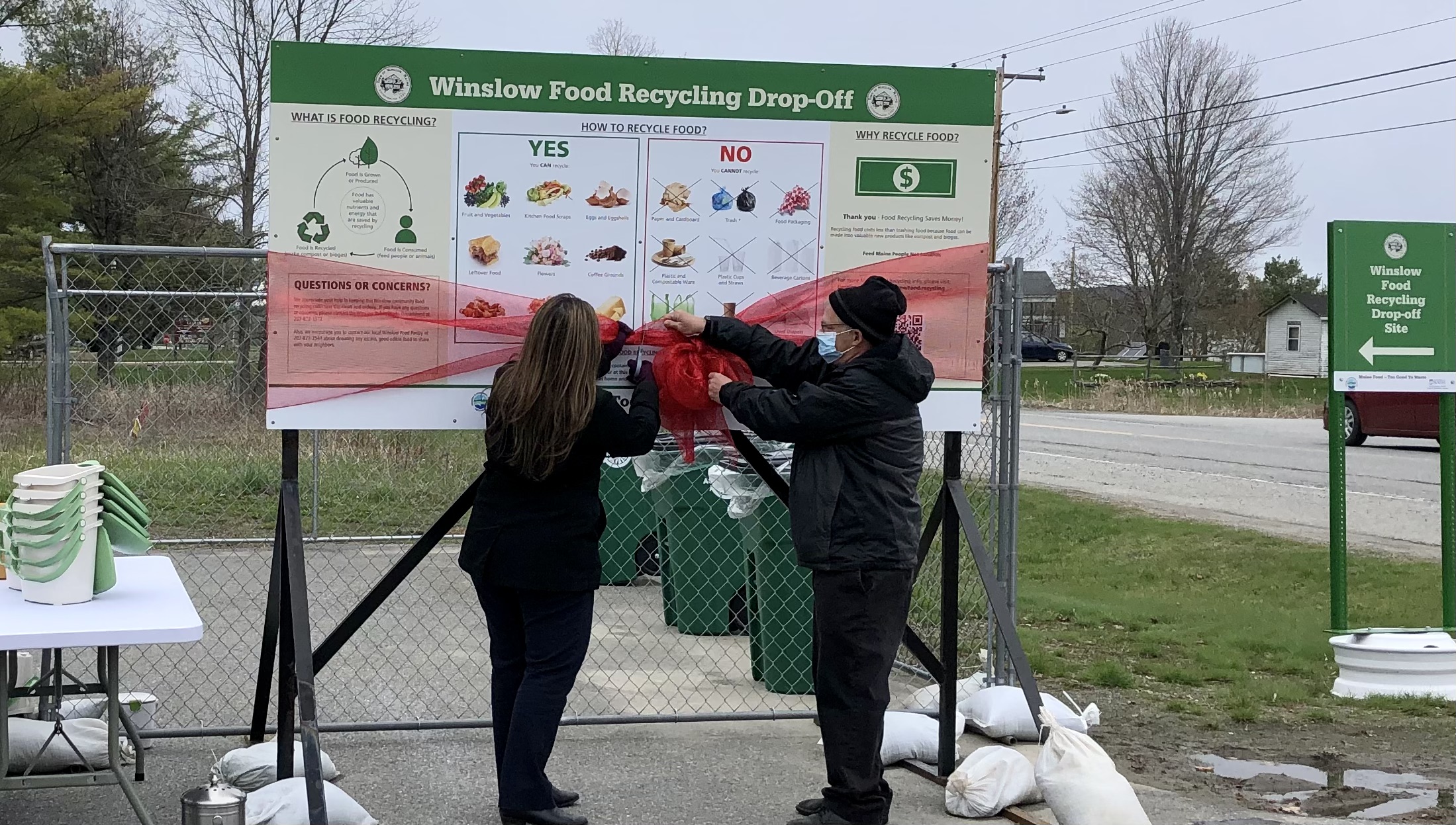 Two people cutting the ribbon on a sign