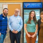 Four people standing in front of UMaine's Community Fridge