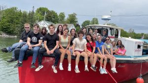 Students sit on the bow of a red boat