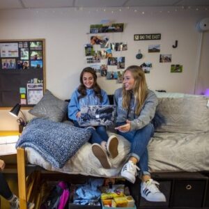 Two people sitting on a bed in a dorm room at UMaine
