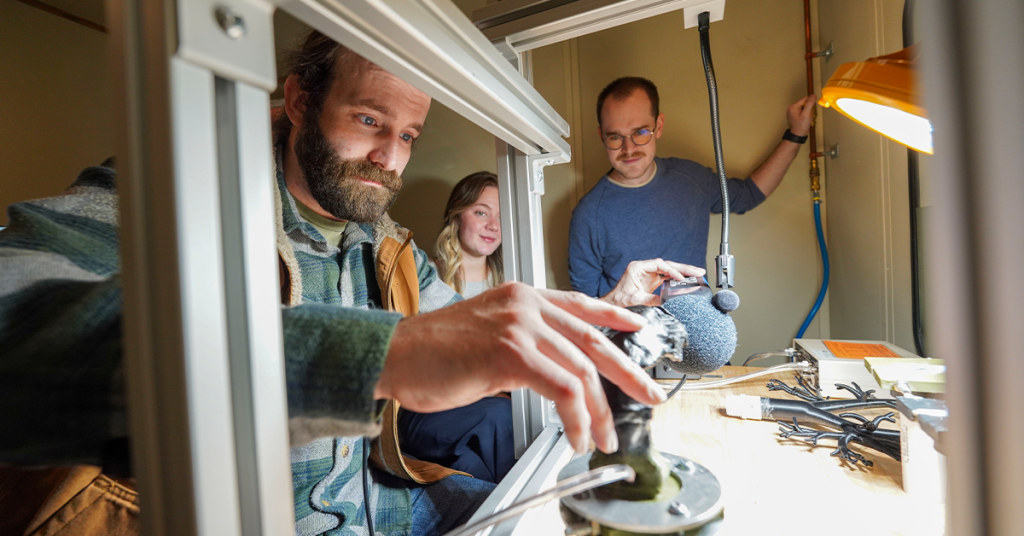 Three students work with audiology equipment in a lab setting