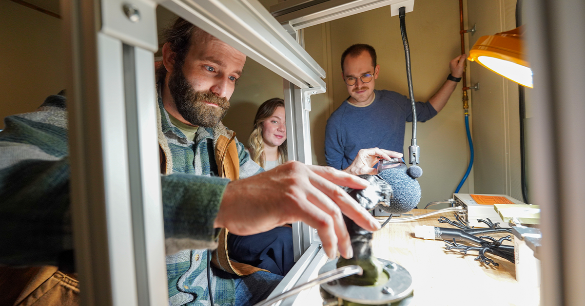 Three students work with audiology equipment in a lab setting
