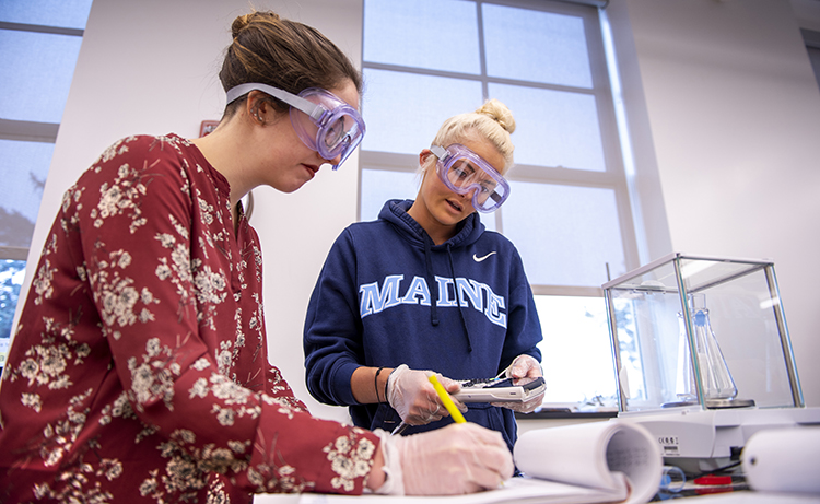 two students working in a lab with protective goggles and gloves