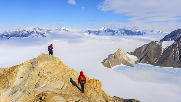 two people standing atop a mountain, wearing hiking gear