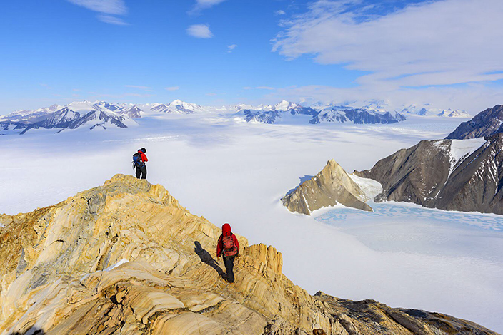 two people standing atop a mountain, wearing hiking gear