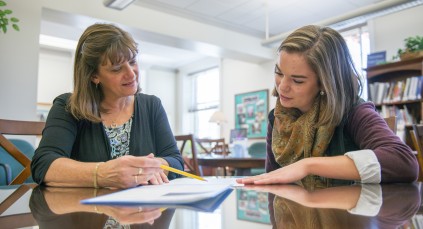 instructor helps student with homework in a library