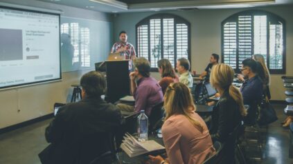 Image of an individual standing at a podium presenting to a room of students