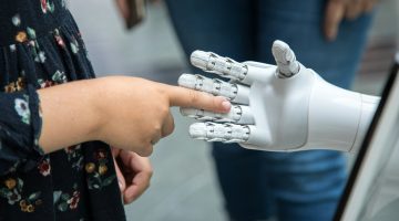 Photo of an open robot hand with a human hand pointing an index finger into the robot hand