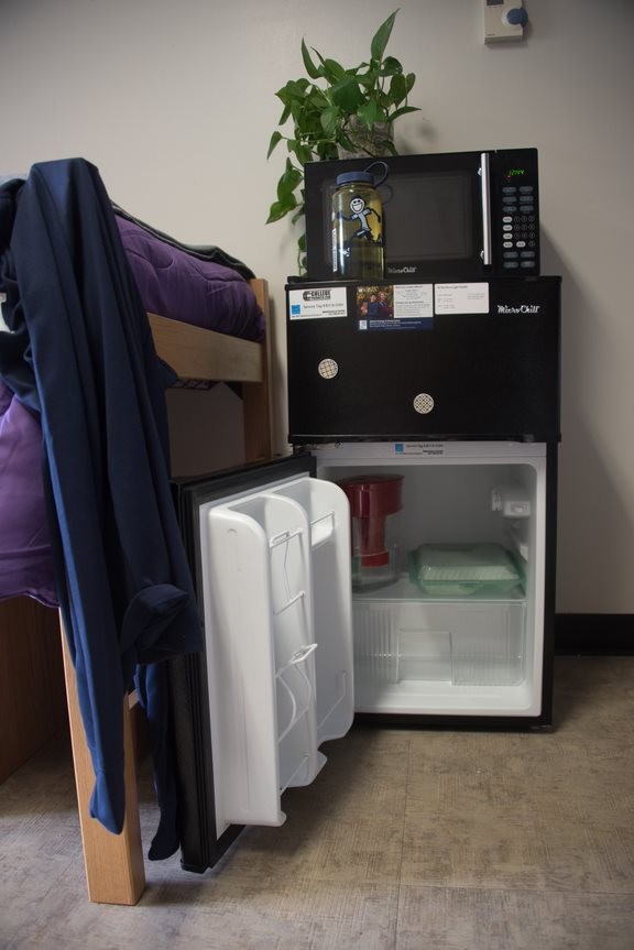 Black MicroChill mini fridge with an open door underneath a microwave in a room.