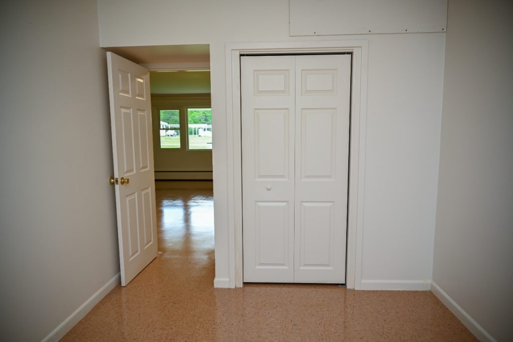 Empty room with a closed white closet door and an open door showing another room.