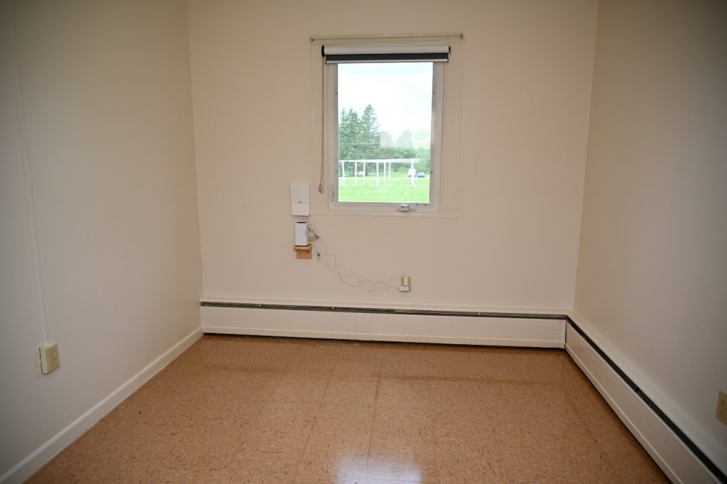 Empty room with a window showing an outdoor field and trees.