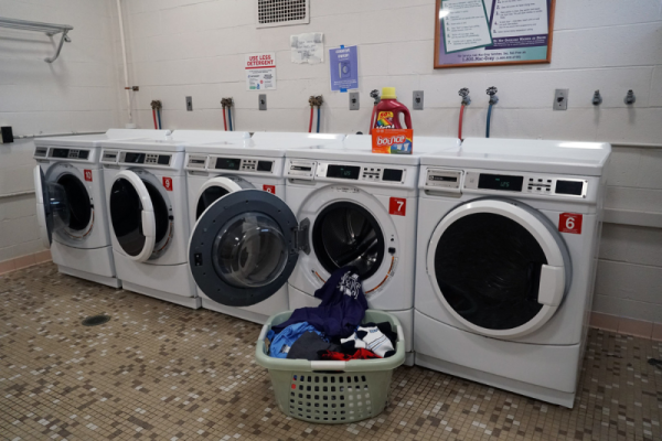 A row of washing machines with a full laundry basket placed in front.