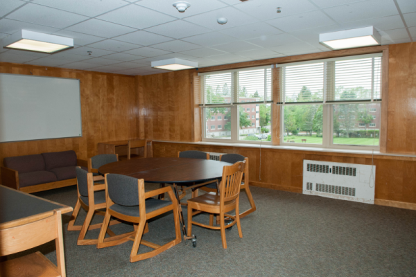 A wood-paneled meeting room with a round conference table, chairs, a whiteboard, and large windows.