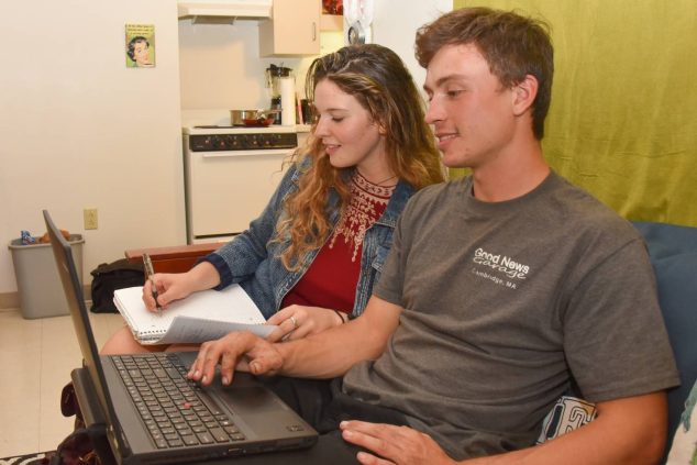 A student using a laptop and another woman writing in a notebook while sitting together.