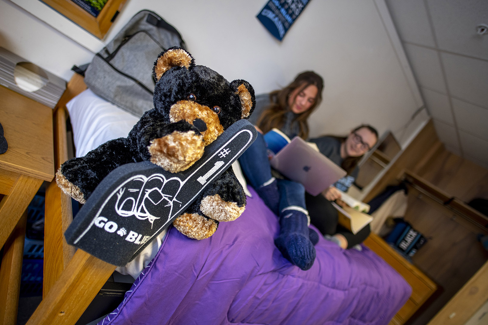 Students sit on a bed with a teddy bear and a foam finger