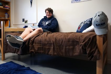 Student sitting on bed in dorm