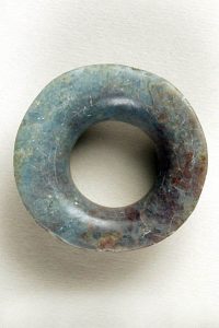 A jade piece of jewelry known as an earflare, it has many different colors which come through in opaline veins and sploches,