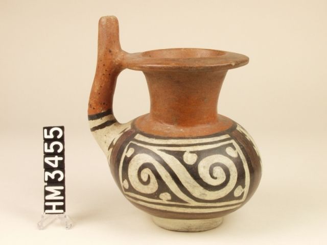 Cocle miniature polychrome ceramic double-spouted jar. This spouted carafe with panels of Y-element profiled heads of pointy-nosed and curly crested creatures may have functioned as a snuffer. The overall Y-element design seems to portray a crested double-headed creature related to a serpent. Suggestions of limb articulations appear as gaps along the body of the serpent.